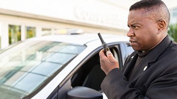 Profissional de segurança utilizando rádio portátil ao lado de um veículo
